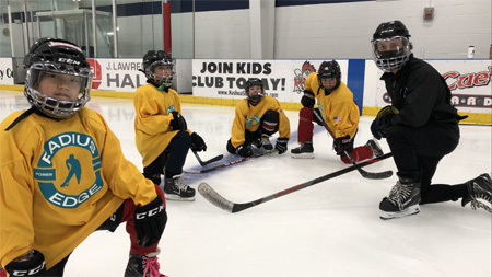 Radiius Edge Power Skating instructor Kyle Greer pauses for a photo opportunity with several younger players at a Radius Edge Power Skating clinic. During the pandemic coaches wore Bauer concept III face shields on top of normal face coverings as a means of player safety.